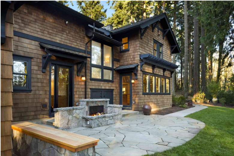 Modern home featuring wood-style exterior home siding options with a stone patio and built-in outdoor fireplace surrounded by a lush forest setting.